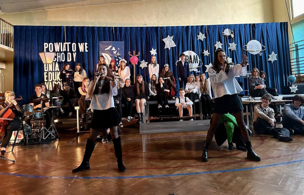 Laura Juchniewicz i Barbara Kosiorek wykonują piosenkę z towarzyszeniem szkolnego zespołu muzycznego