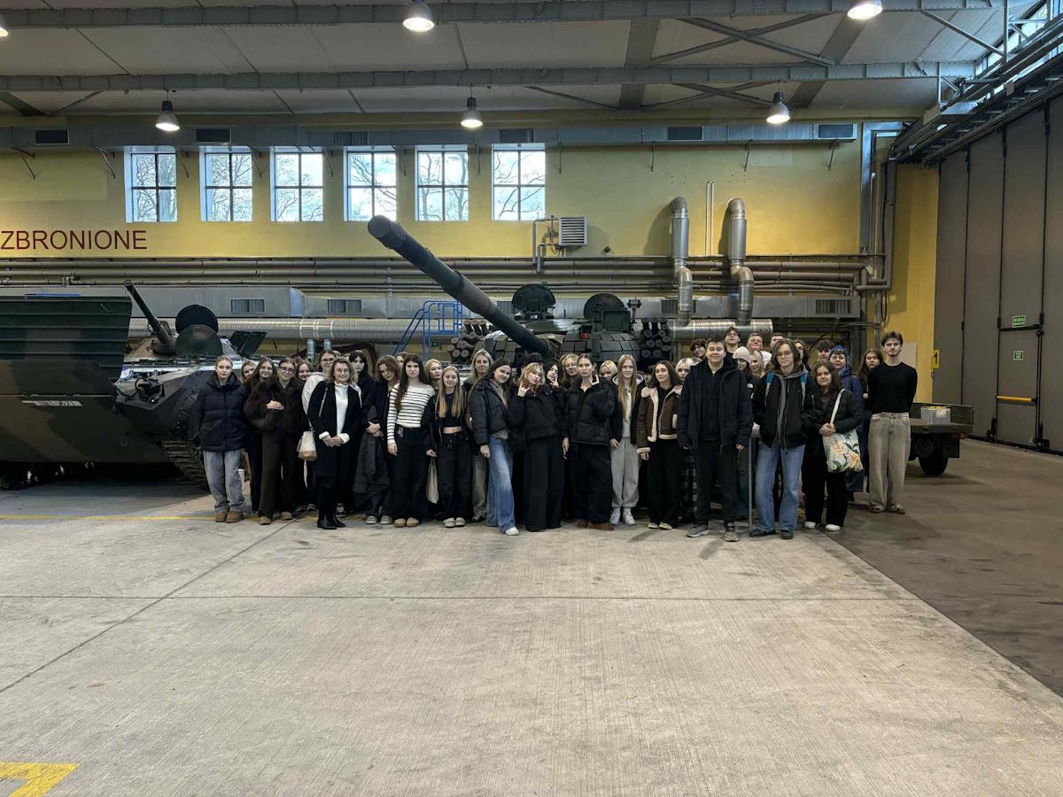 Uczestnicy wycieczki na tle czołgu i transportera opancerzonego